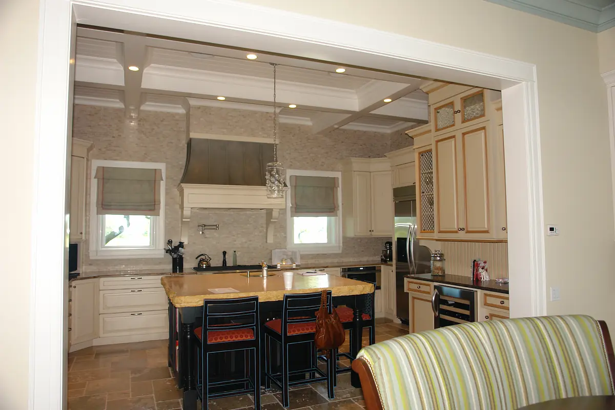 Kitchen with island, stone countertop, bar stools, light cabinetry, and stainless steel appliances.