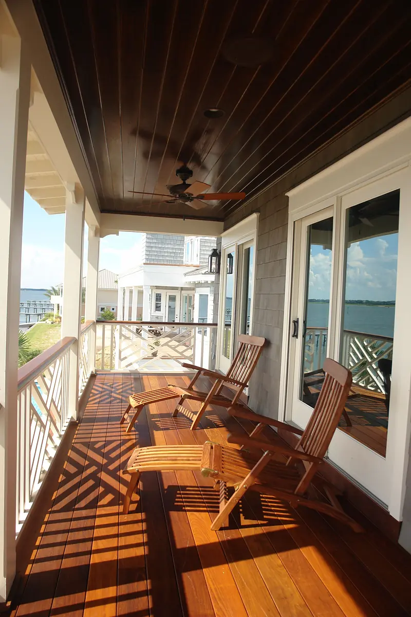 Deck with wooden lounge chairs, railing, wooden planks, and a ceiling fan.