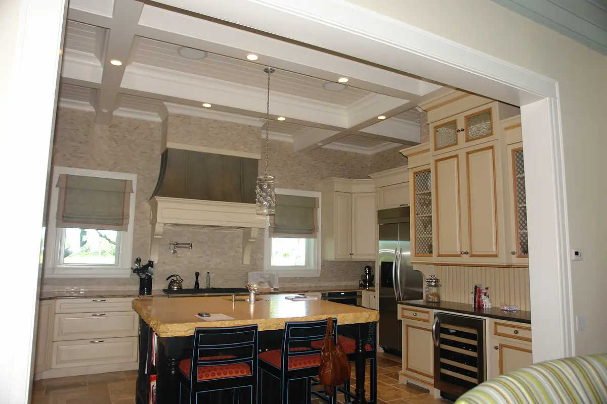 Kitchen with island, bar stools, stainless steel appliances, stone backsplash, and wooden cabinetry.