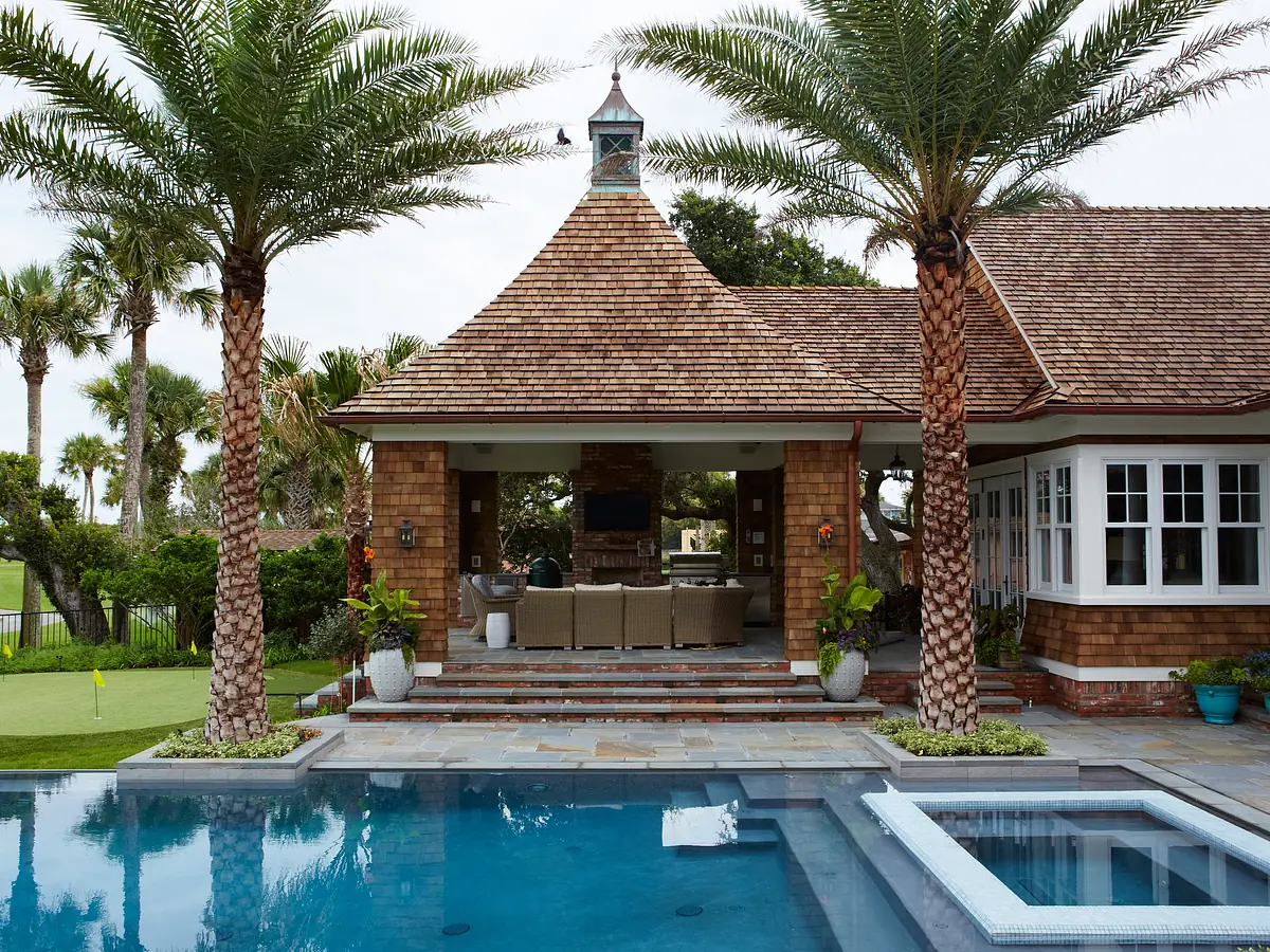 Exterior space with swimming pool, stone patio, palm trees, house with large windows, and outdoor seating area.