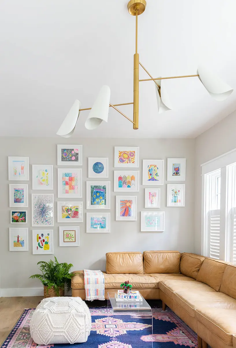 Living room with brown leather sectional, white coffee table, area rug, framed artworks, and multi-arm chandelier.