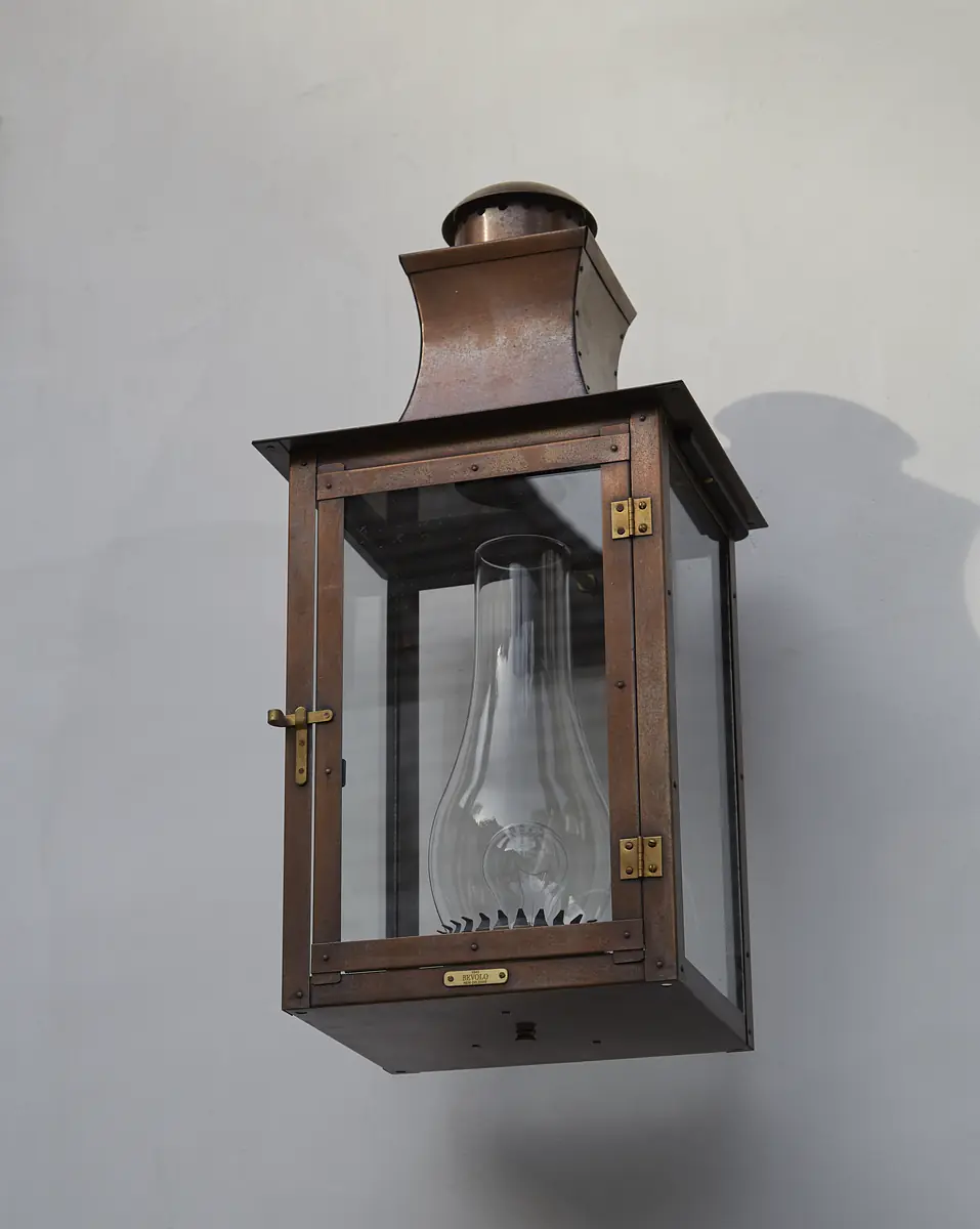 Wall-mounted lantern with metal frame, glass enclosure, and conical top.