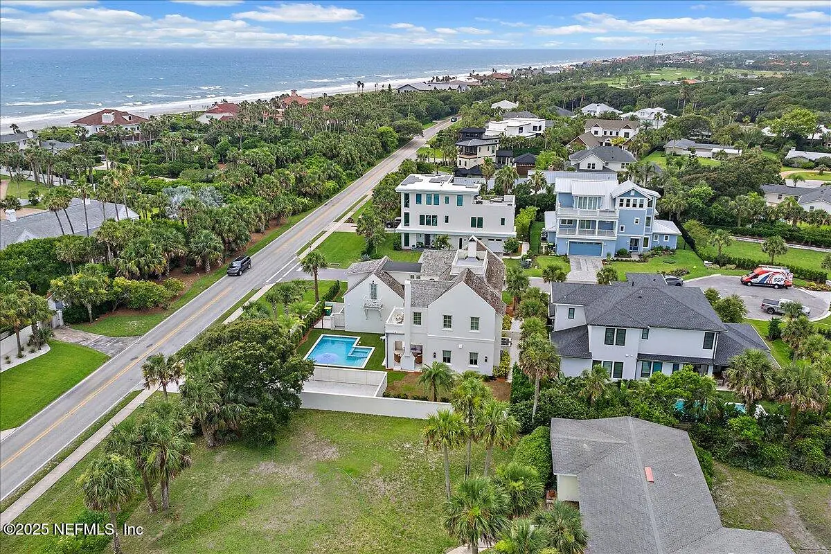 Aerial view of coastal residential area with houses, a road, and beach.