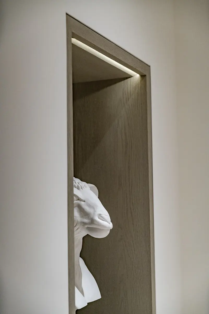 Niche with white bust sculpture on light wood shelf and recessed lighting above.