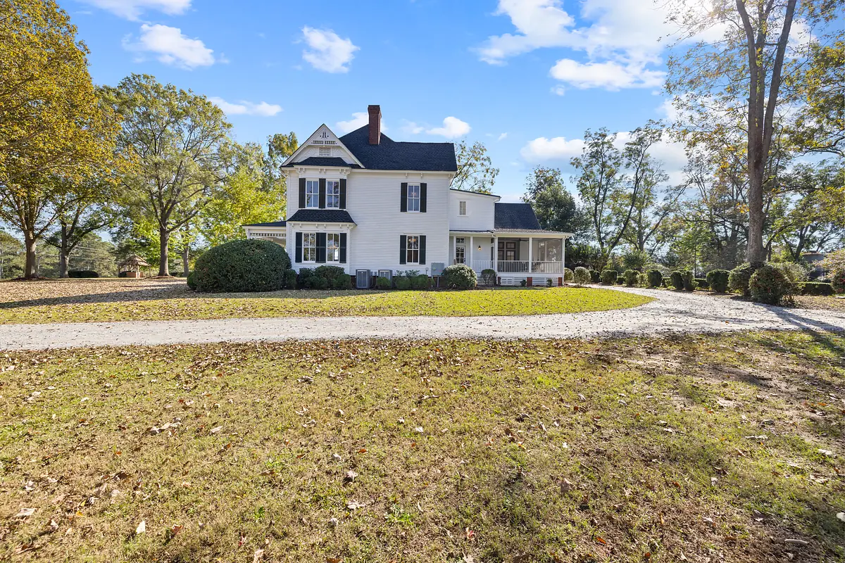 Two-story house with gabled roof, white siding, black shutters, front porch, and landscaped yard