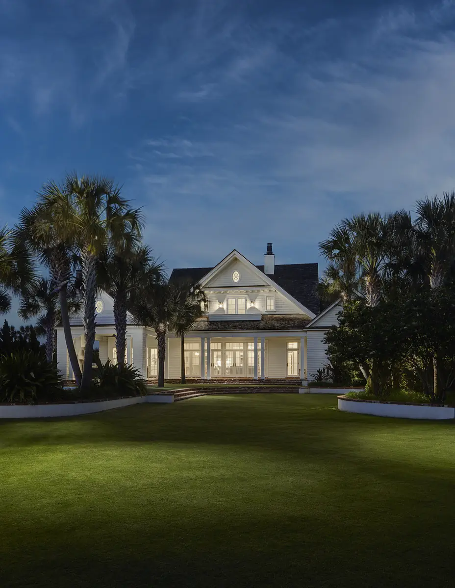 Front exterior of a house with white siding, large windows, palm trees, and well-maintained lawn.