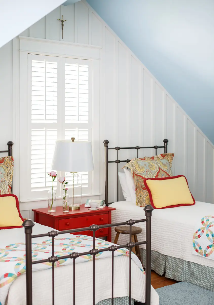 Bedroom with two metal framed beds, patterned quilts, red nightstand, and a sloped ceiling with window