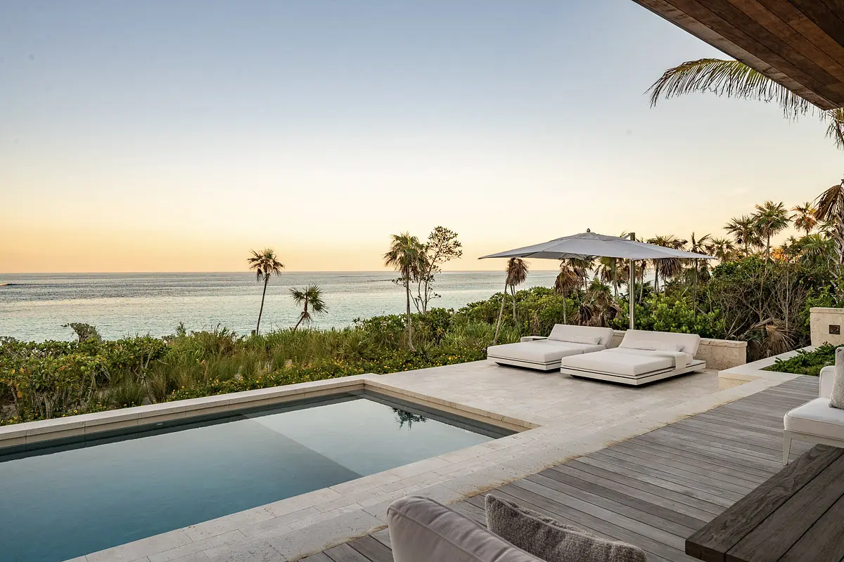 Outdoor deck with white lounge chairs, umbrella, swimming pool, and ocean views.