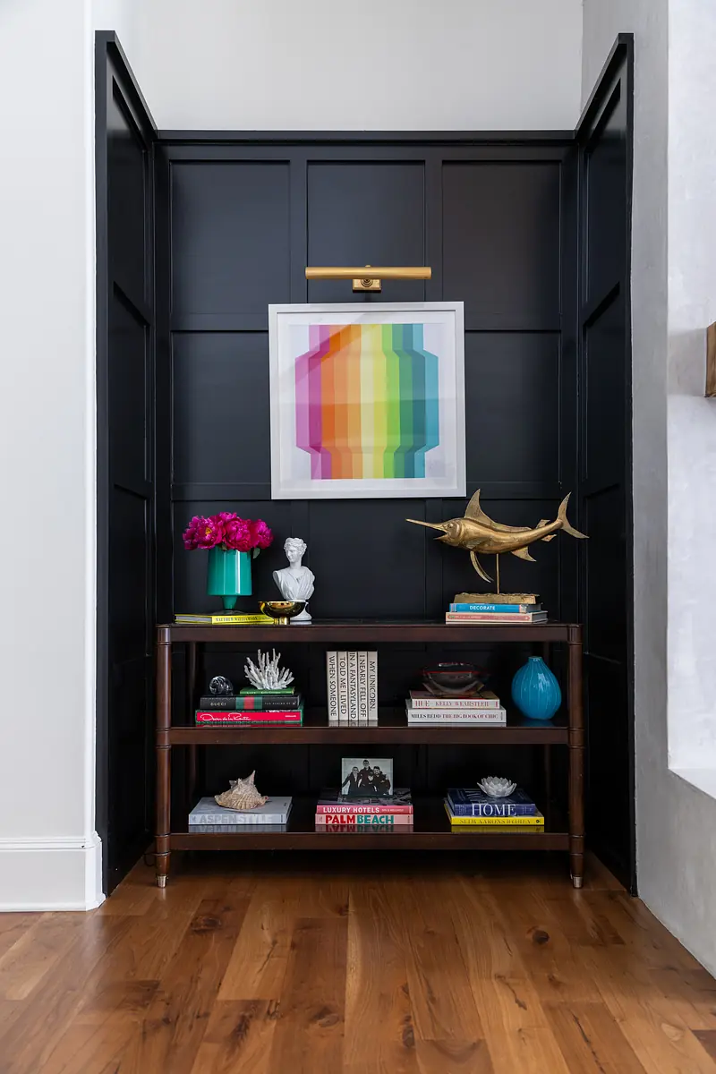 Display nook with wooden shelves, colorful artwork, books, and decorative objects against dark paneled walls.