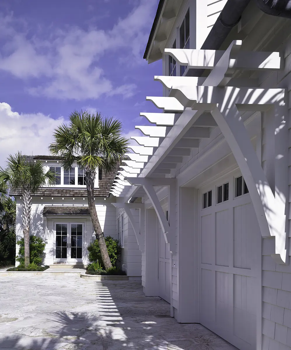 Exterior front view of a house with white siding, garage doors, stone pathway, porch, and palm trees.