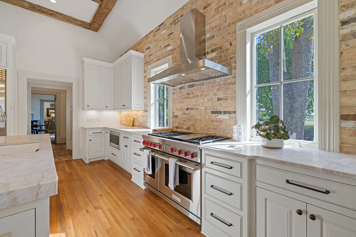 Kitchen with white cabinetry, stainless steel stove, marble countertop, brick wall, and large windows
