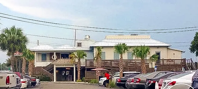Exterior front of a multi-level building with wooden deck, metal roof, palm trees, and parking area.