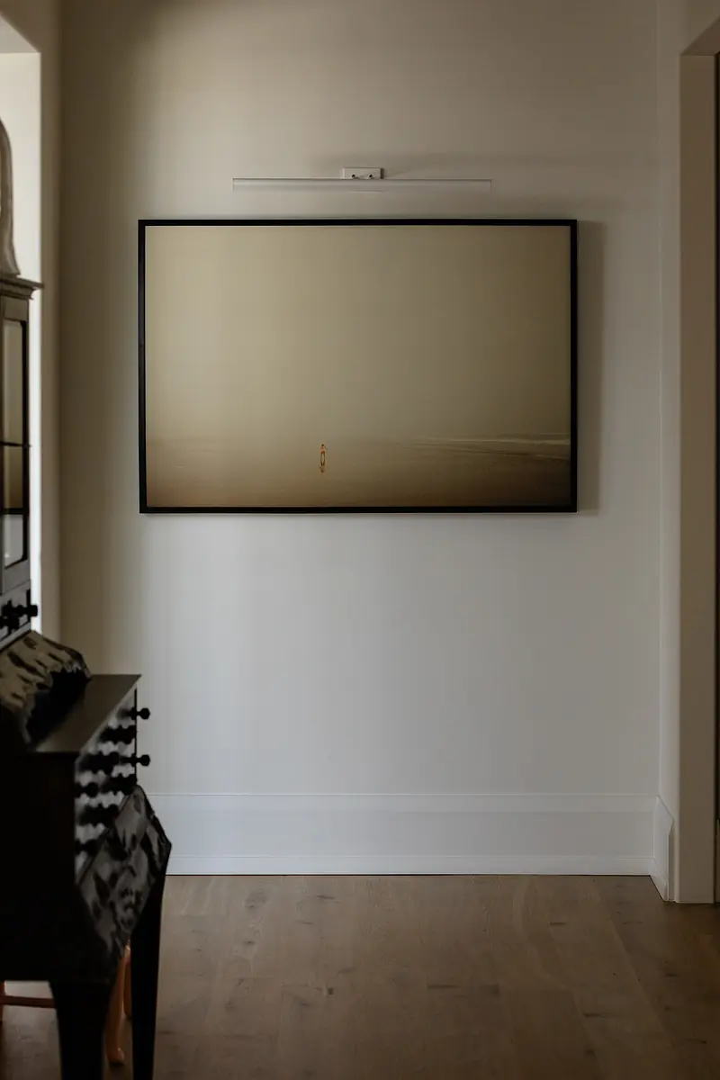 Empty wall with large framed artwork and dark wood furniture in foreground.