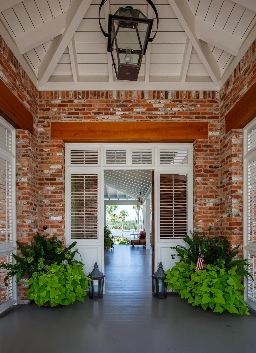 Foyer with rustic brick wall, white double doors, greenery, wooden beams, and lantern fixture