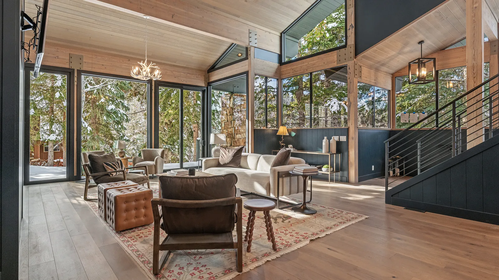 Living room with white sofa, brown chairs, rug, large windows, wooden ceiling, and staircase.
