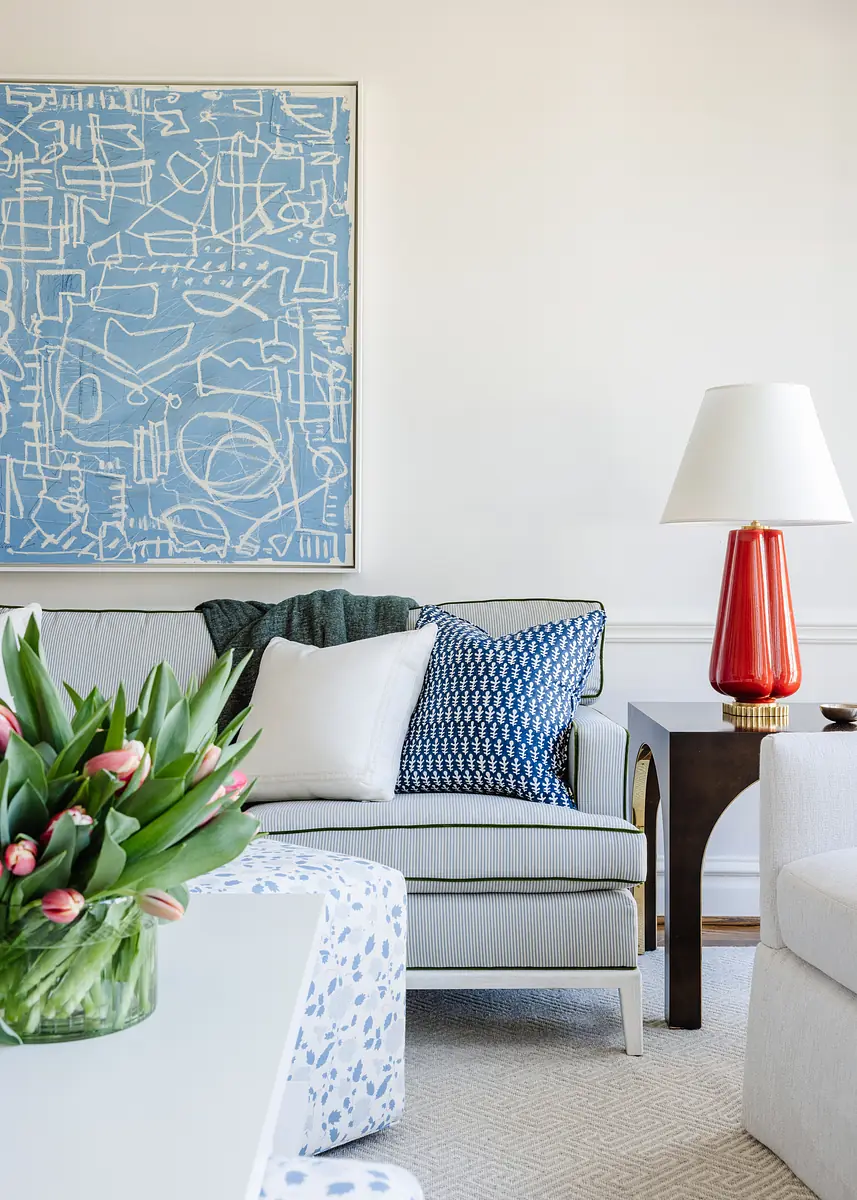 Living room with gray sofa, white coffee table, red lamp, tulip bouquet, and blue abstract painting.