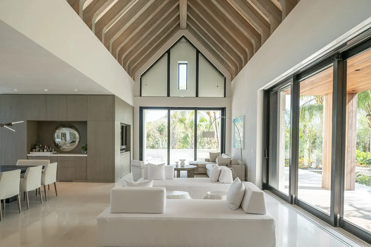 Living room with two white sofas, white coffee table, high ceiling, and large glass doors to outdoor area
