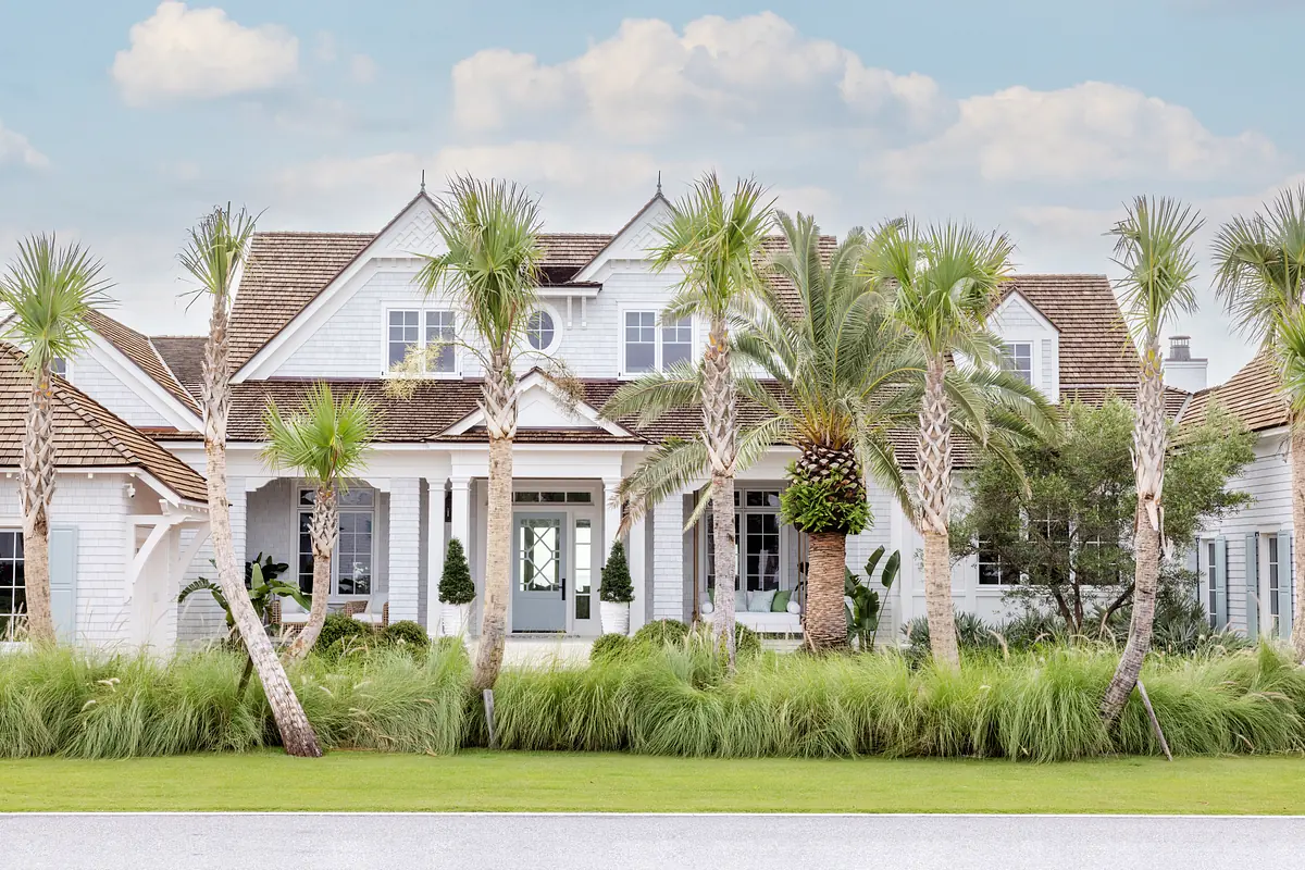 House exterior with central door, gabled roofs, palm trees, ornamental grasses, and a well-manicured lawn.