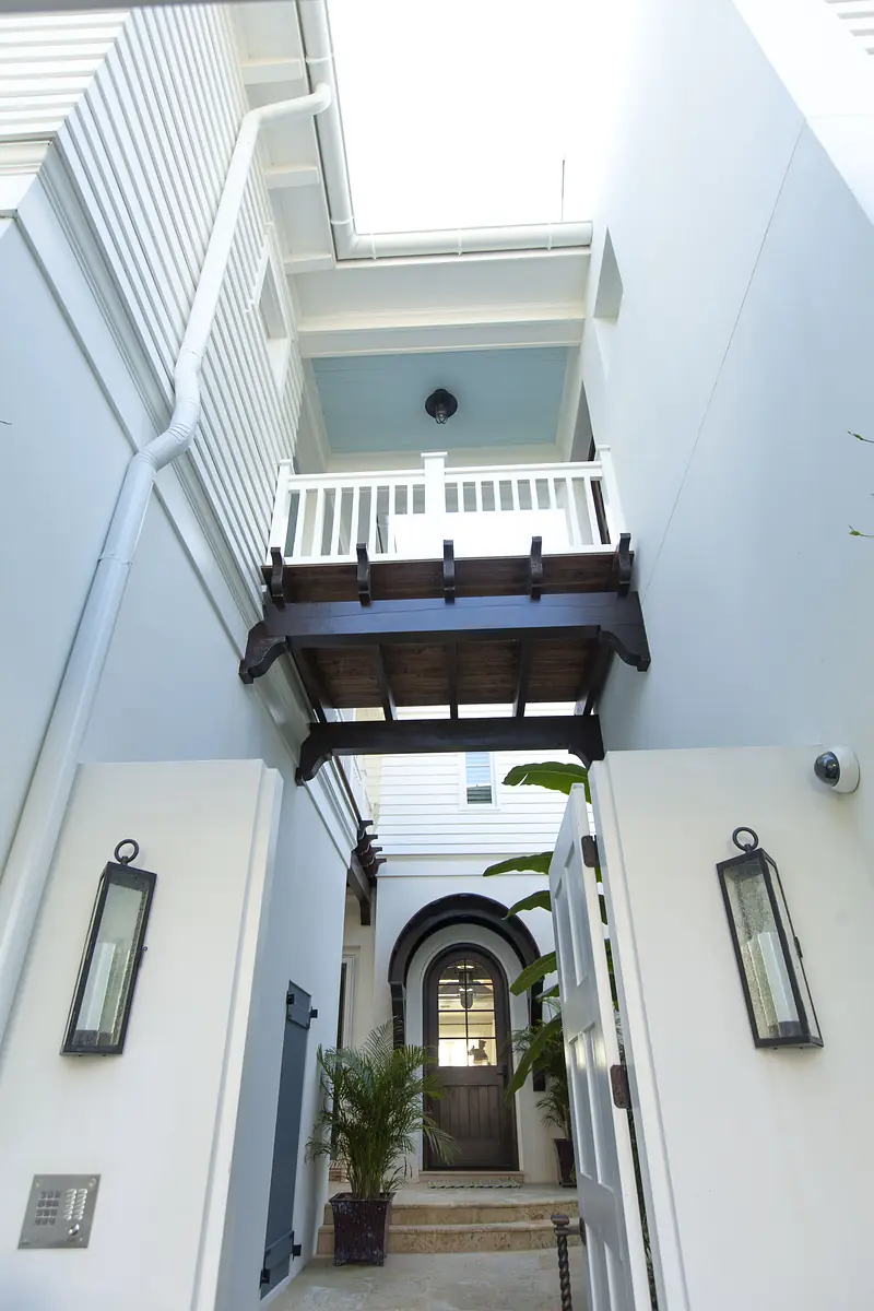 Exterior entrance with wooden balcony, arched doorway, two lanterns, and a palm plant.