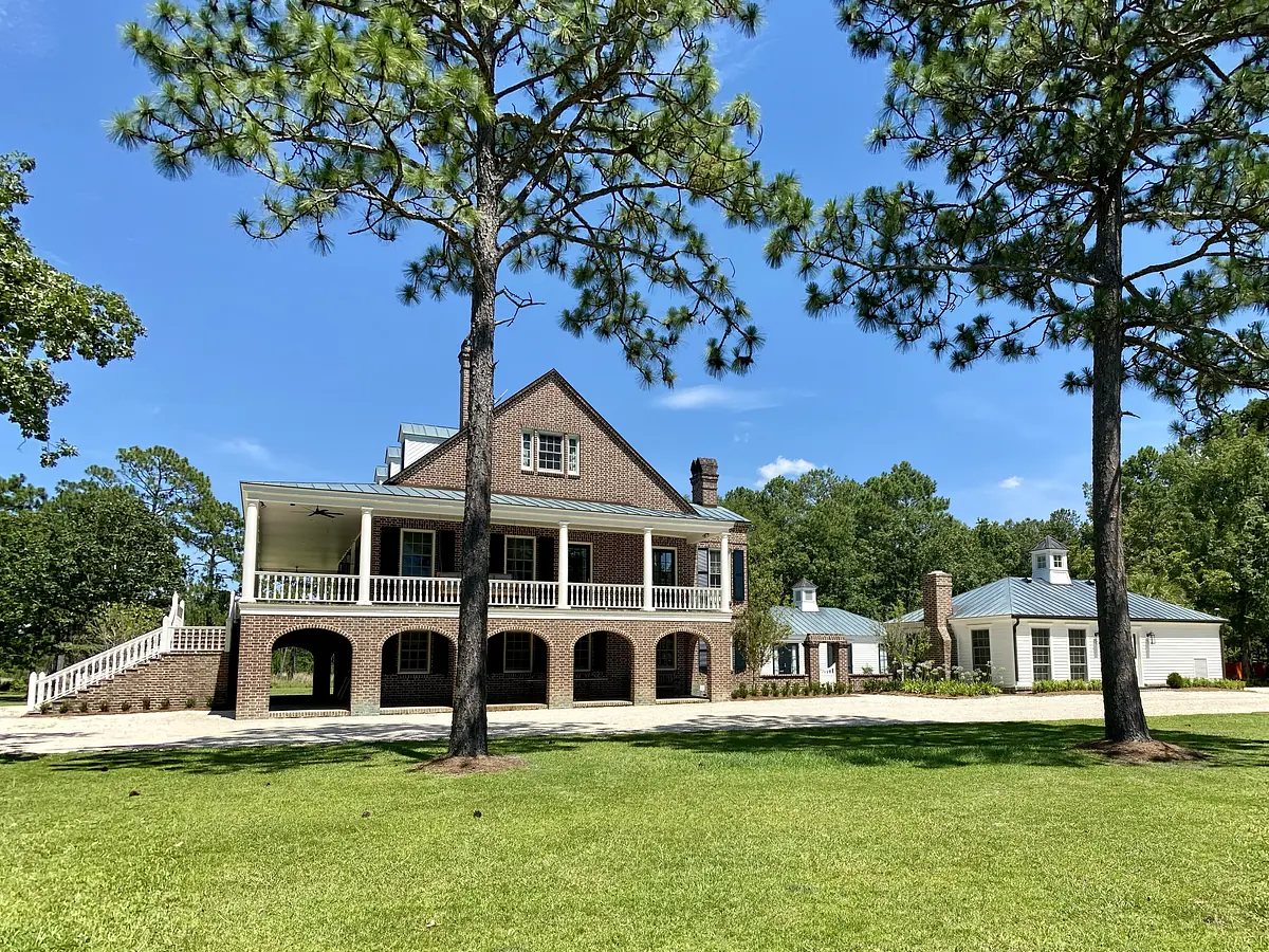 Exterior front of a two-story brick house with porch, lawn, and tall pine trees.