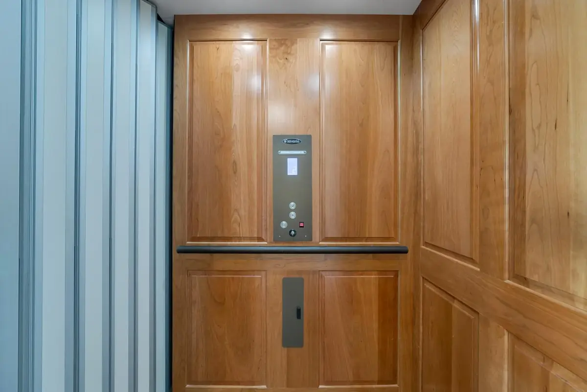 Elevator with wooden wall panels, control panel, and metallic door latch.