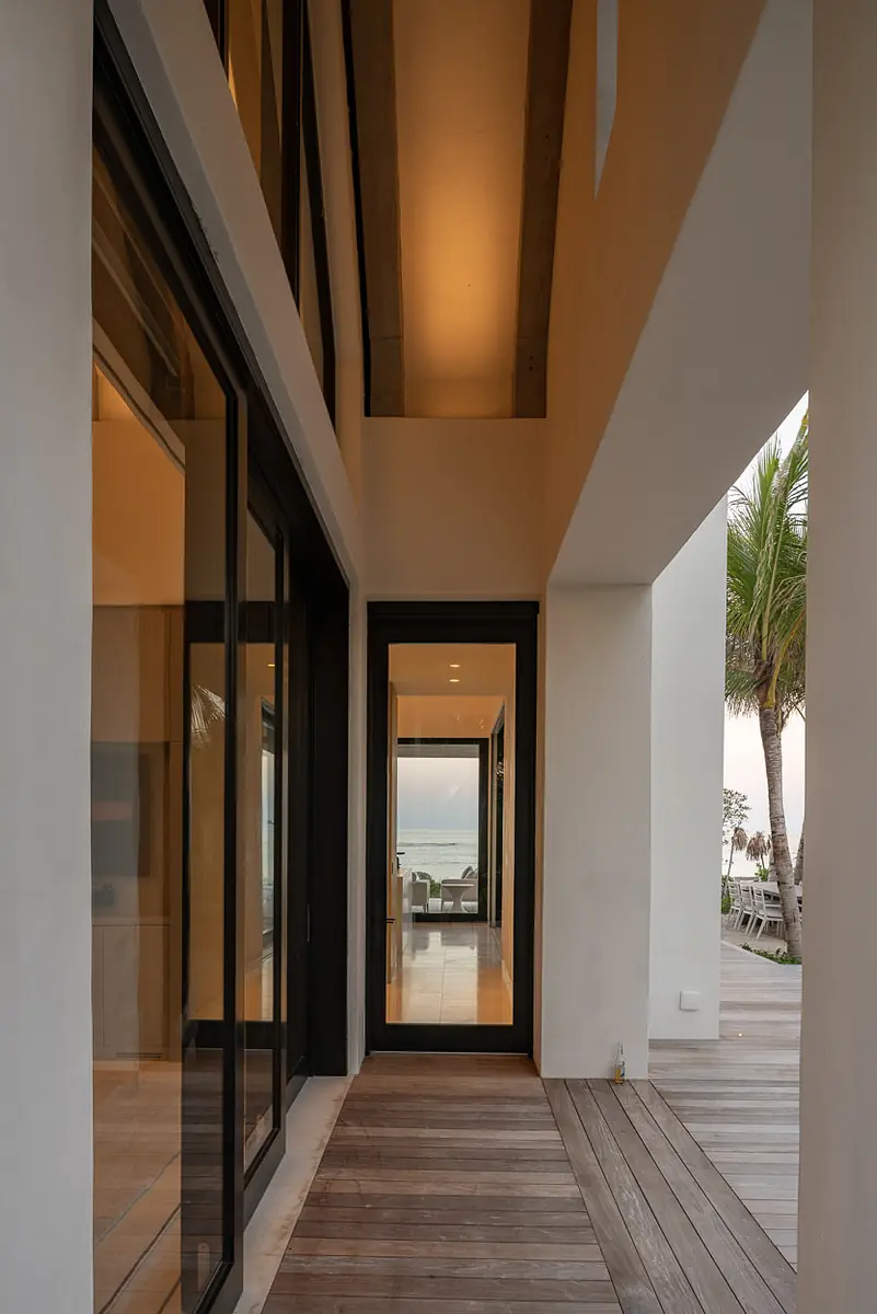 Hallway with glass doors, wooden flooring, and natural light leading to another door.