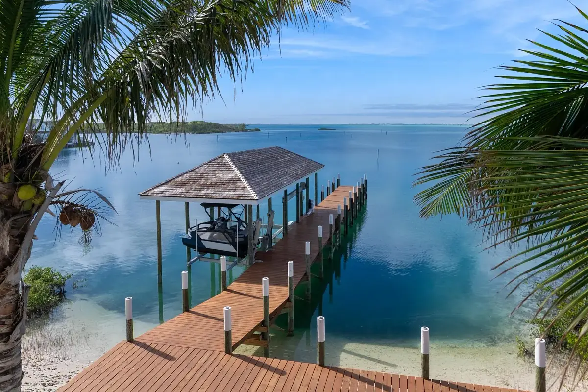 Deck over water with wooden planks, small pavilion, palm trees, and clear blue water