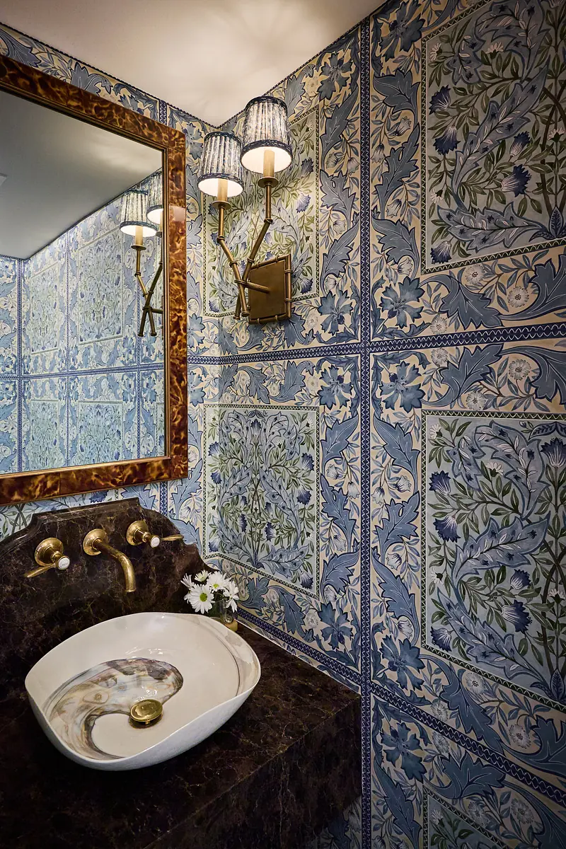 Powder room with floral wallpaper, marble sink, ornate mirror, and wall sconce.