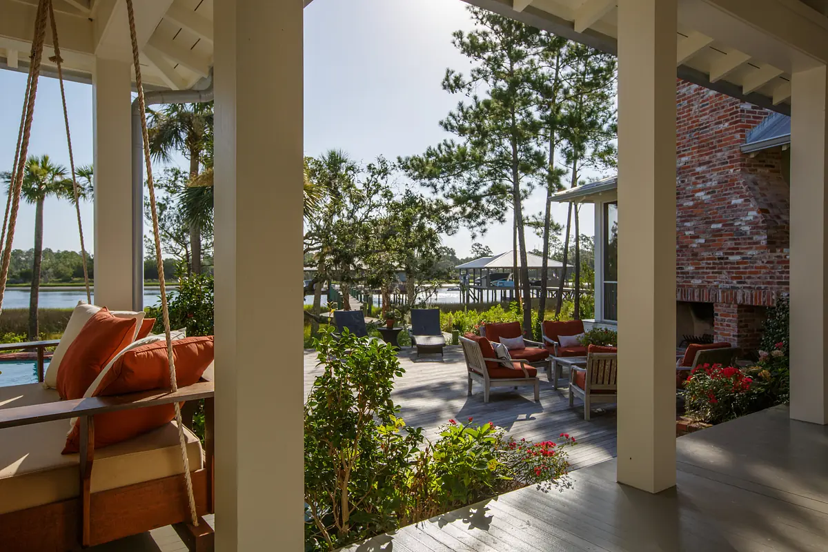 Outdoor deck with lounge chairs, wooden swing, and built-in fireplace overlooking water.