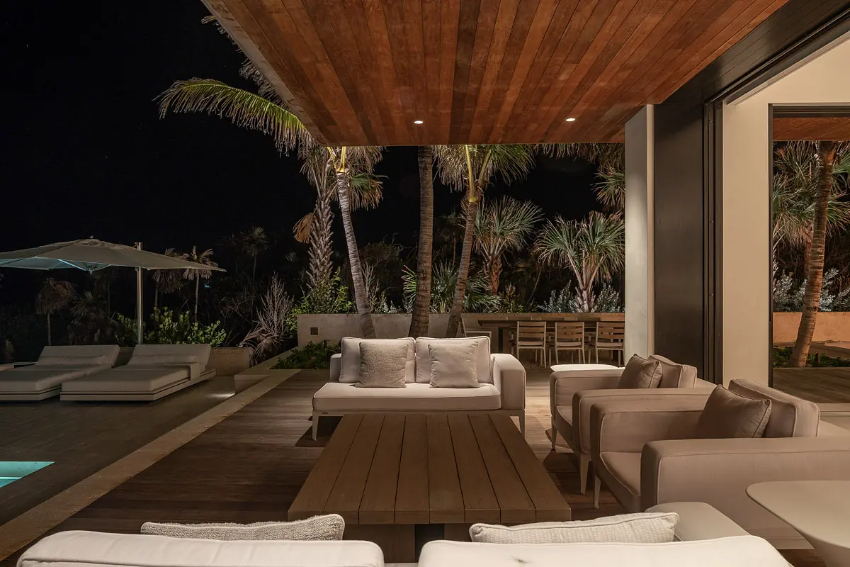 Deck with white outdoor sofas, wooden coffee table, dining area, palm trees, and pool.