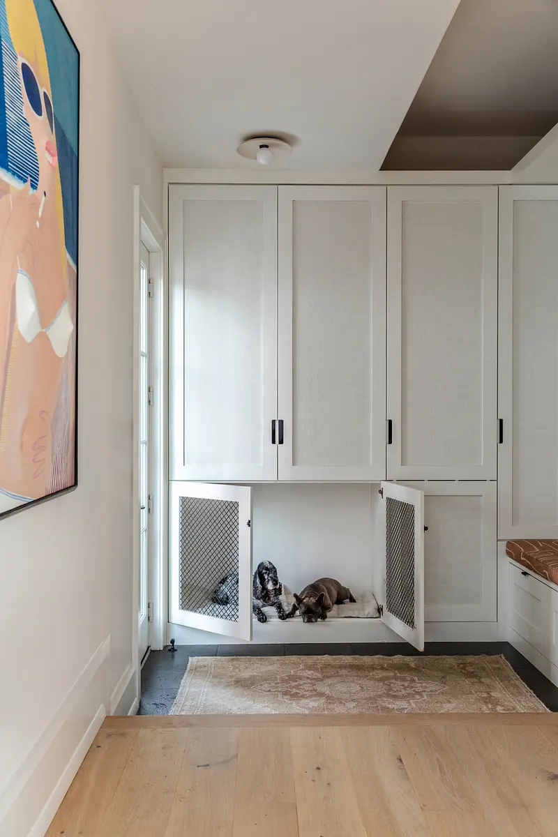 Mudroom with white cabinetry, pet bed, area rug, and large wall art, featuring a door leading outside.