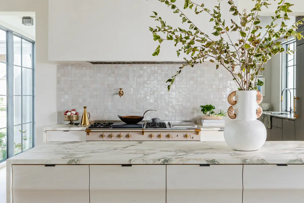 Kitchen with marble island, gas stovetop, white tile backsplash, and a large vase with branches