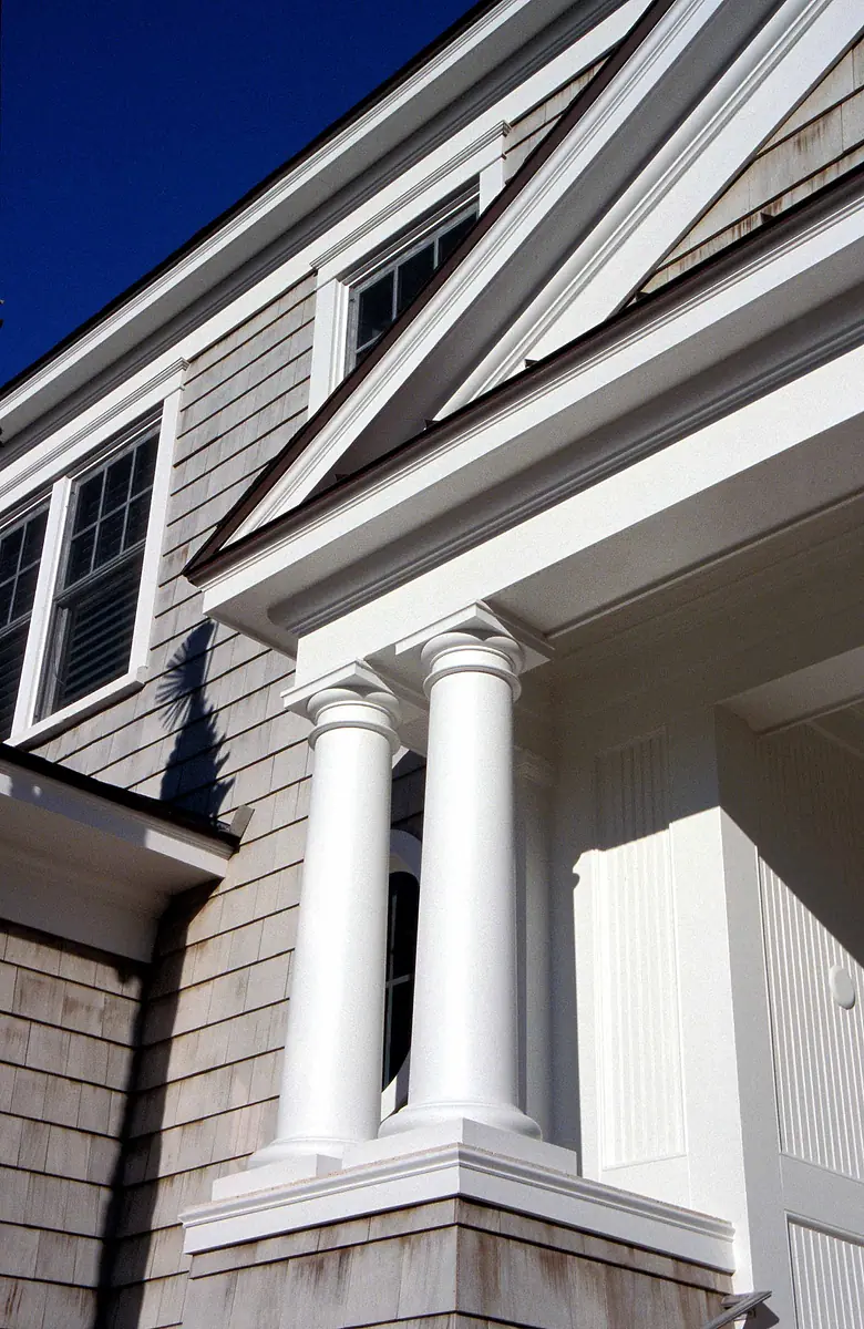 Front exterior of a house with white columns, shingles, windows, and a gable roof.