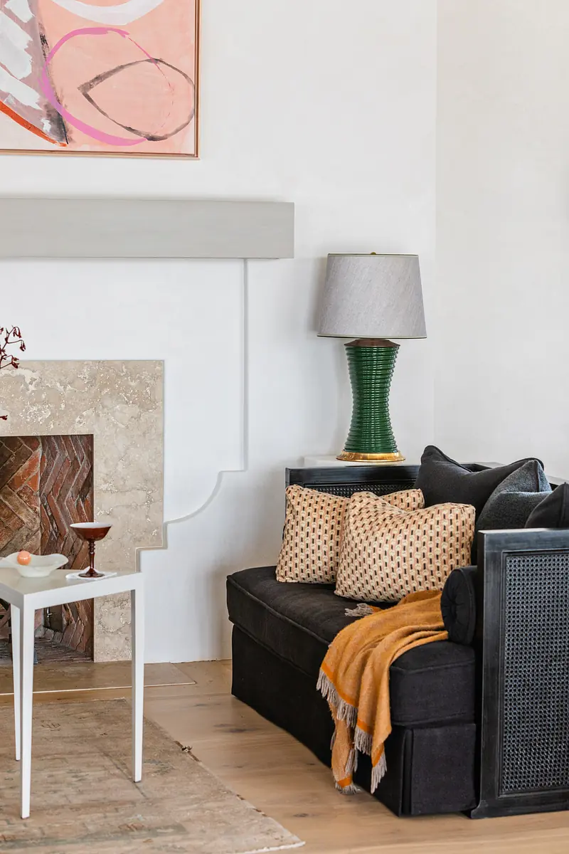 Living room with black sectional sofa, decorated side table, lamp, area rug, beige stone fireplace, and abstract art.