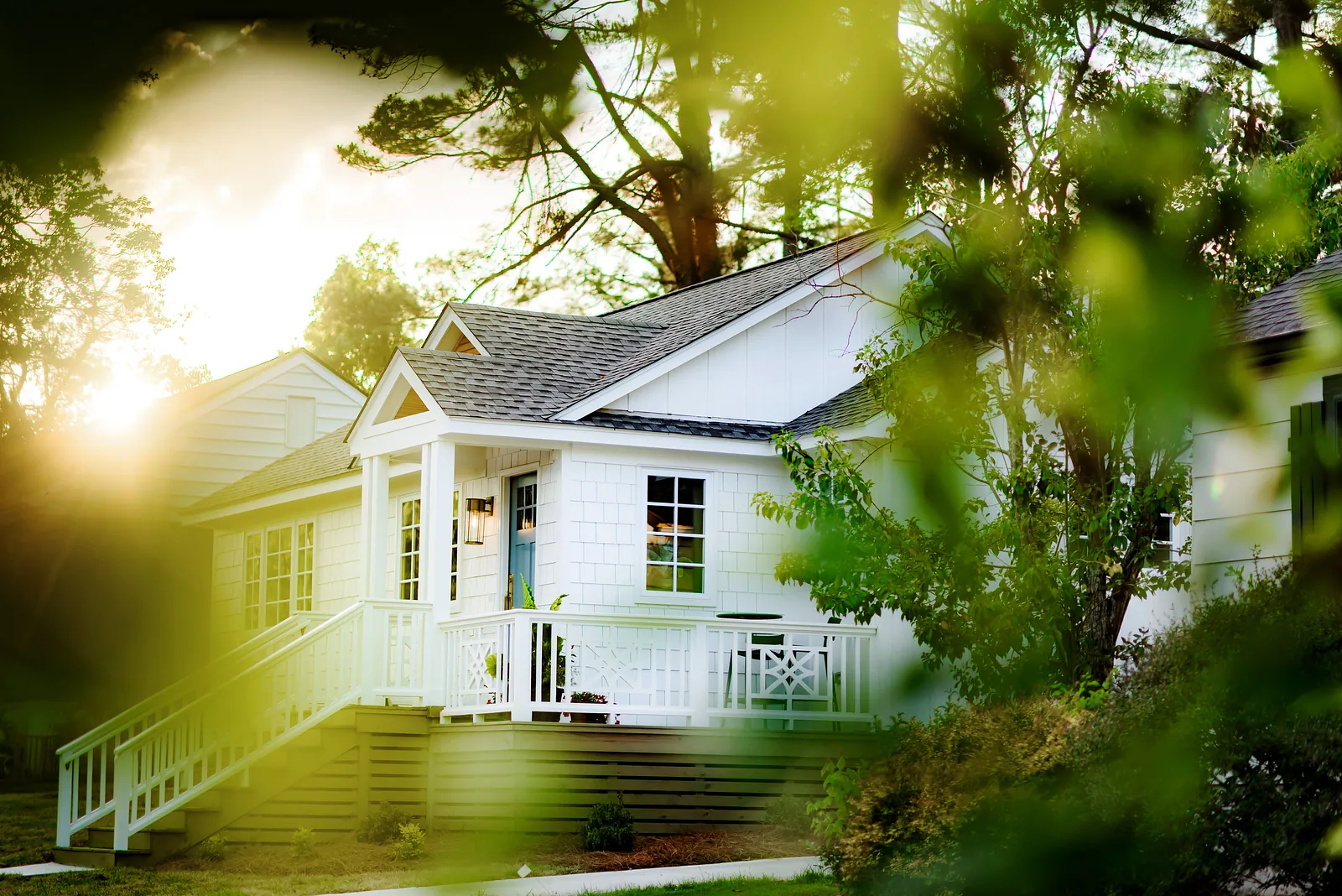 Front exterior view of a house with white façade, gray roof, and wooden porch in a green setting.