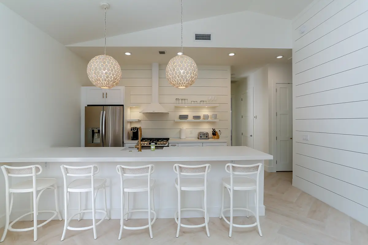 Kitchen with white countertop, bar stools, stainless steel refrigerator, gas stove, and open shelving.