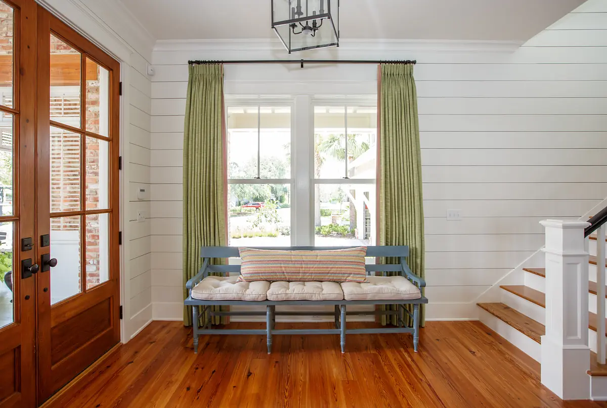 Foyer with blue bench, wooden flooring, large windows, green curtains, and staircase.
