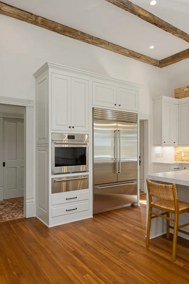 Kitchen with white cabinetry, stainless steel appliances, hardwood floor, island, and wooden stool.