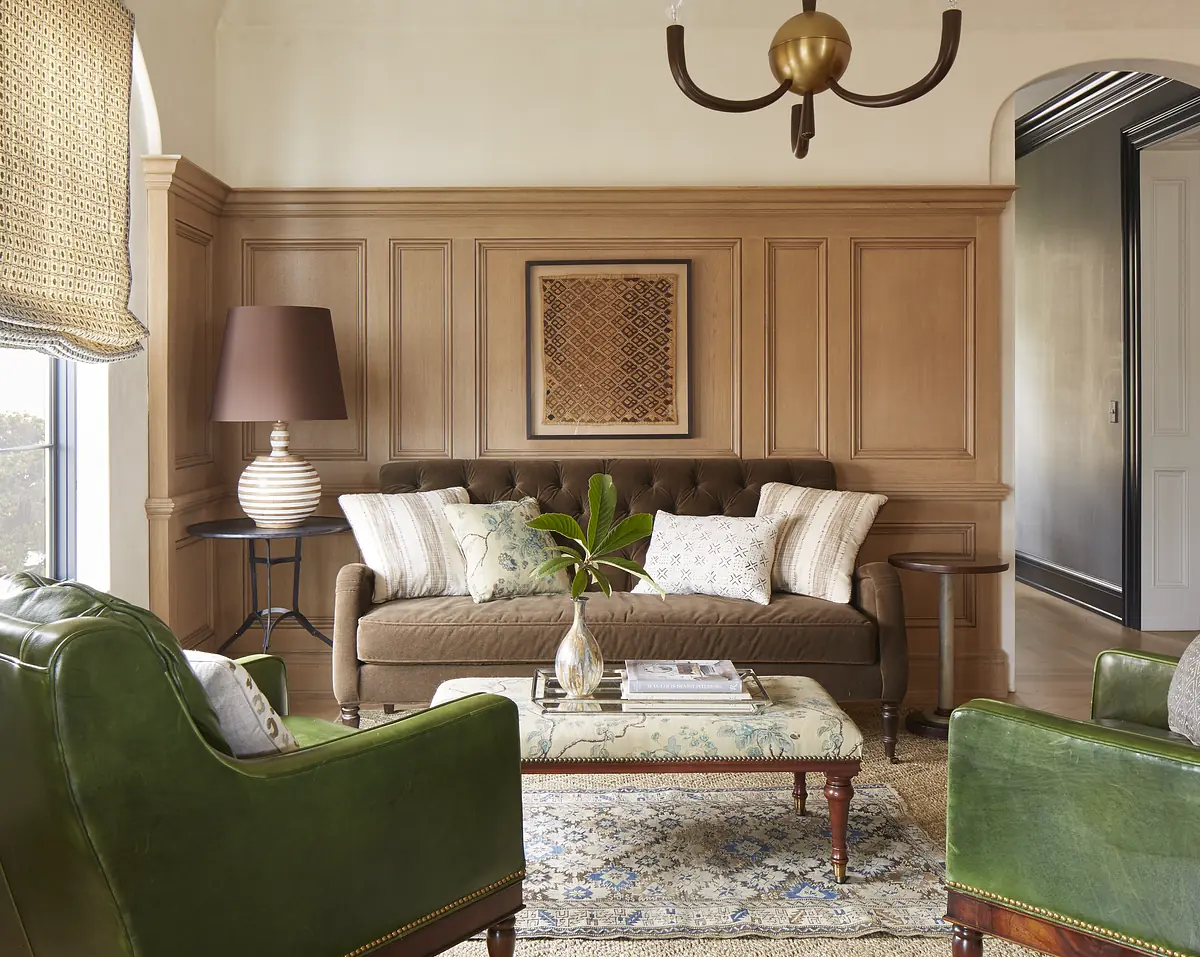 Living room with brown sofa, green armchairs, round coffee table, area rug, and wood paneling.