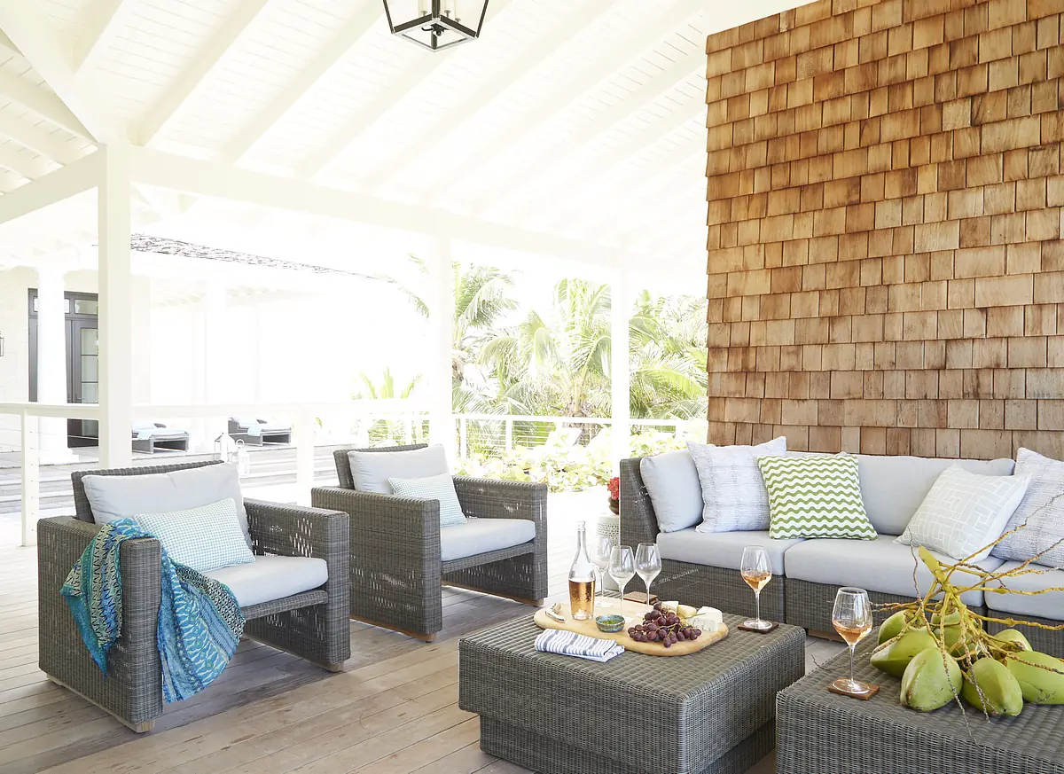 Patio with wicker chairs, sectional sofa, coffee table, and greenery in the background.