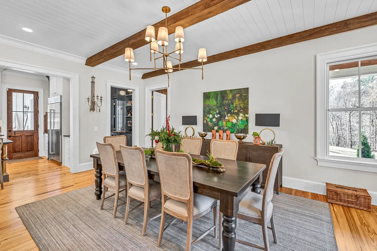 Dining room with long wood table, nine seats, chandelier, sideboards, large windows, and exposed beams
