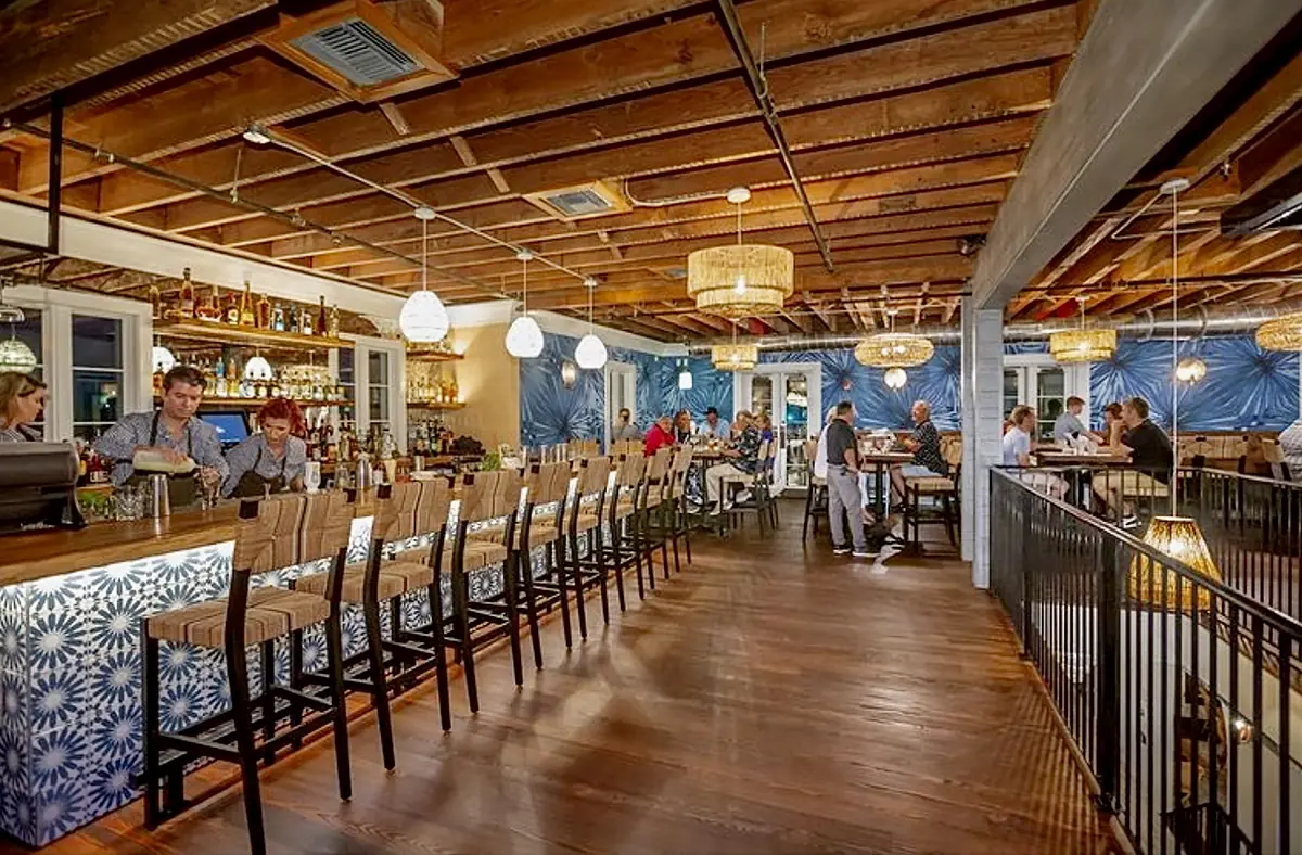 Dining room with bar, tables, chairs, wooden ceiling, and decorative lights, featuring a blue patterned wall.
