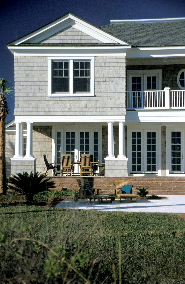 Exterior rear view with porch, rocking chairs, chaise lounges, gray shingle siding, and landscaping.