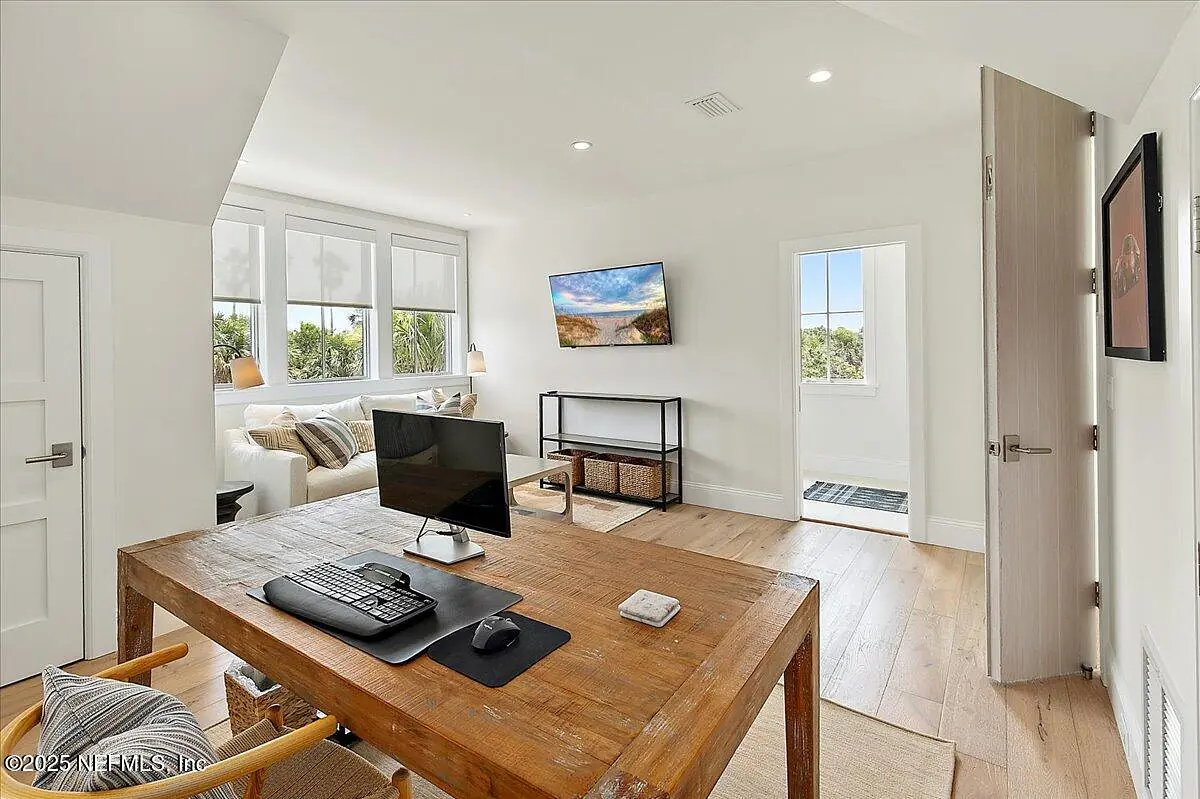 Office with wooden desk, computer, sofa, television, and large windows for natural light.