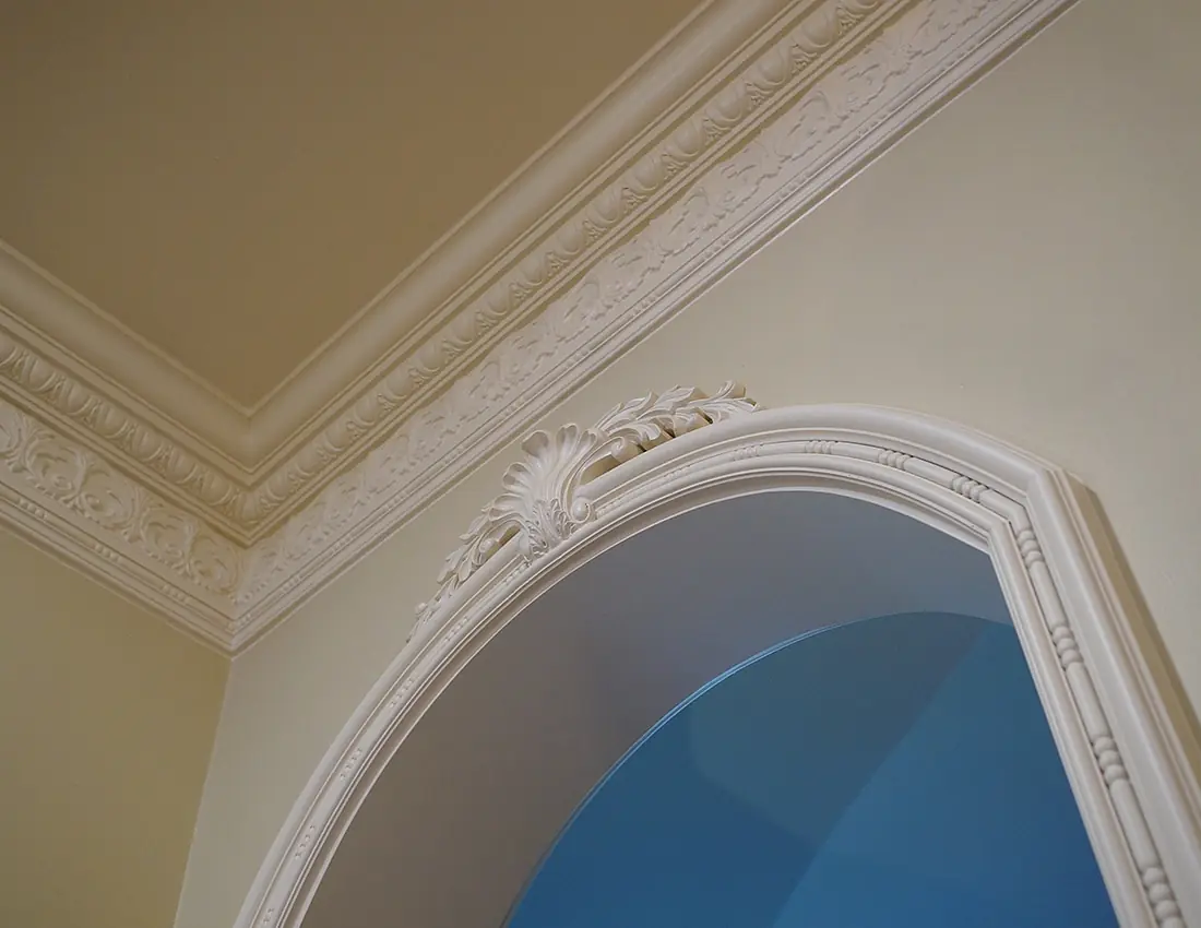 Architectural detail with archway, decorative trim, blue wall, and ornate ceiling molding.