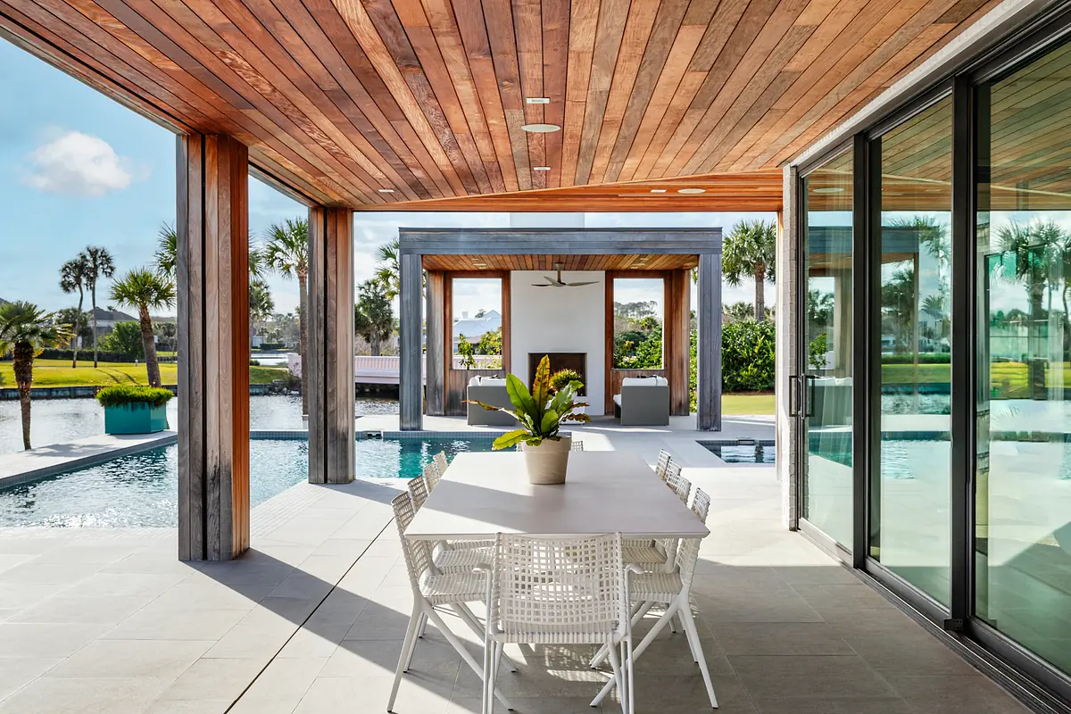 Outdoor patio with dining table, white chairs, potted plant, sliding doors, and pool view