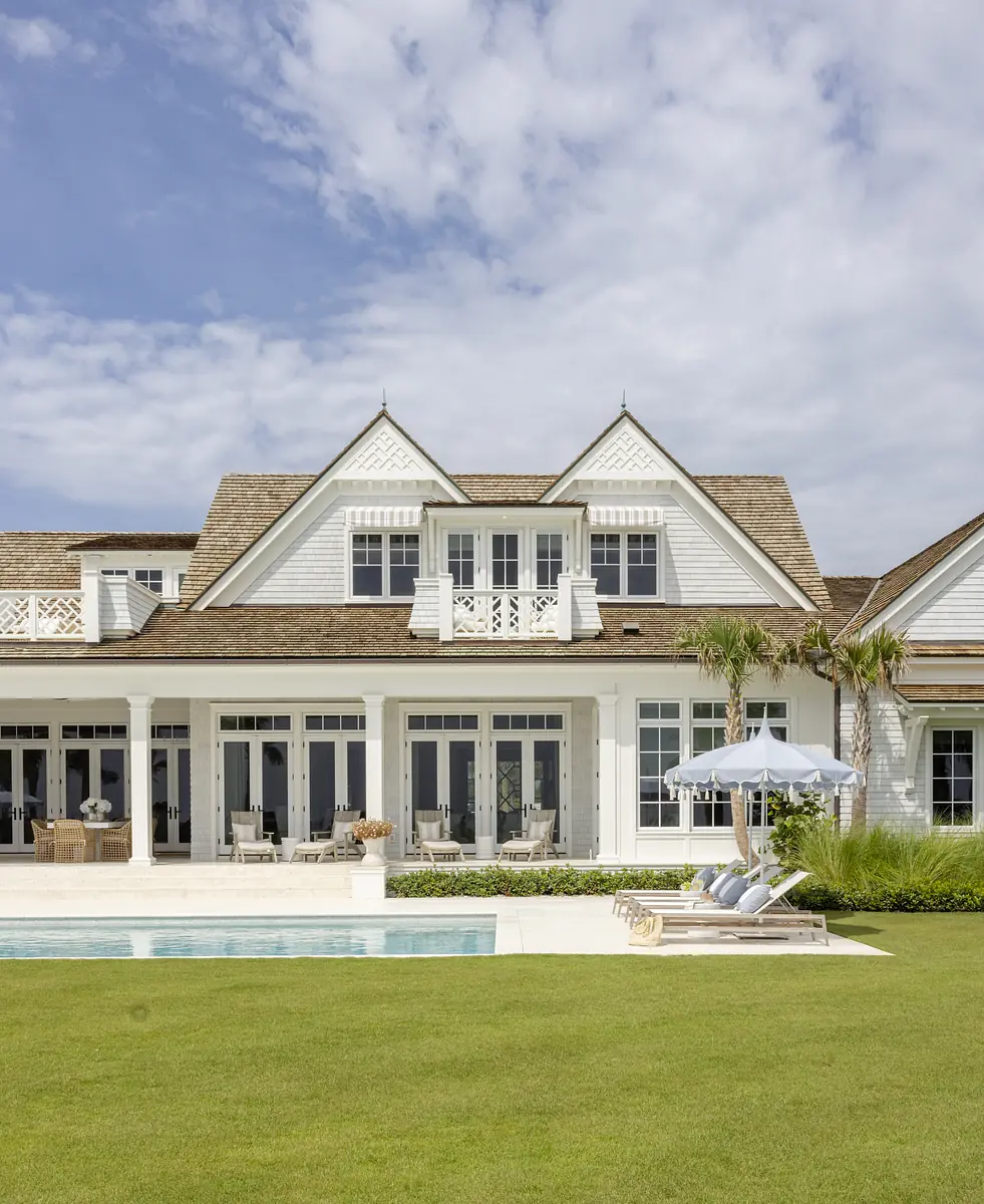 Exterior rear of a house with large windows, swimming pool, outdoor lounge chairs, and a white umbrella.