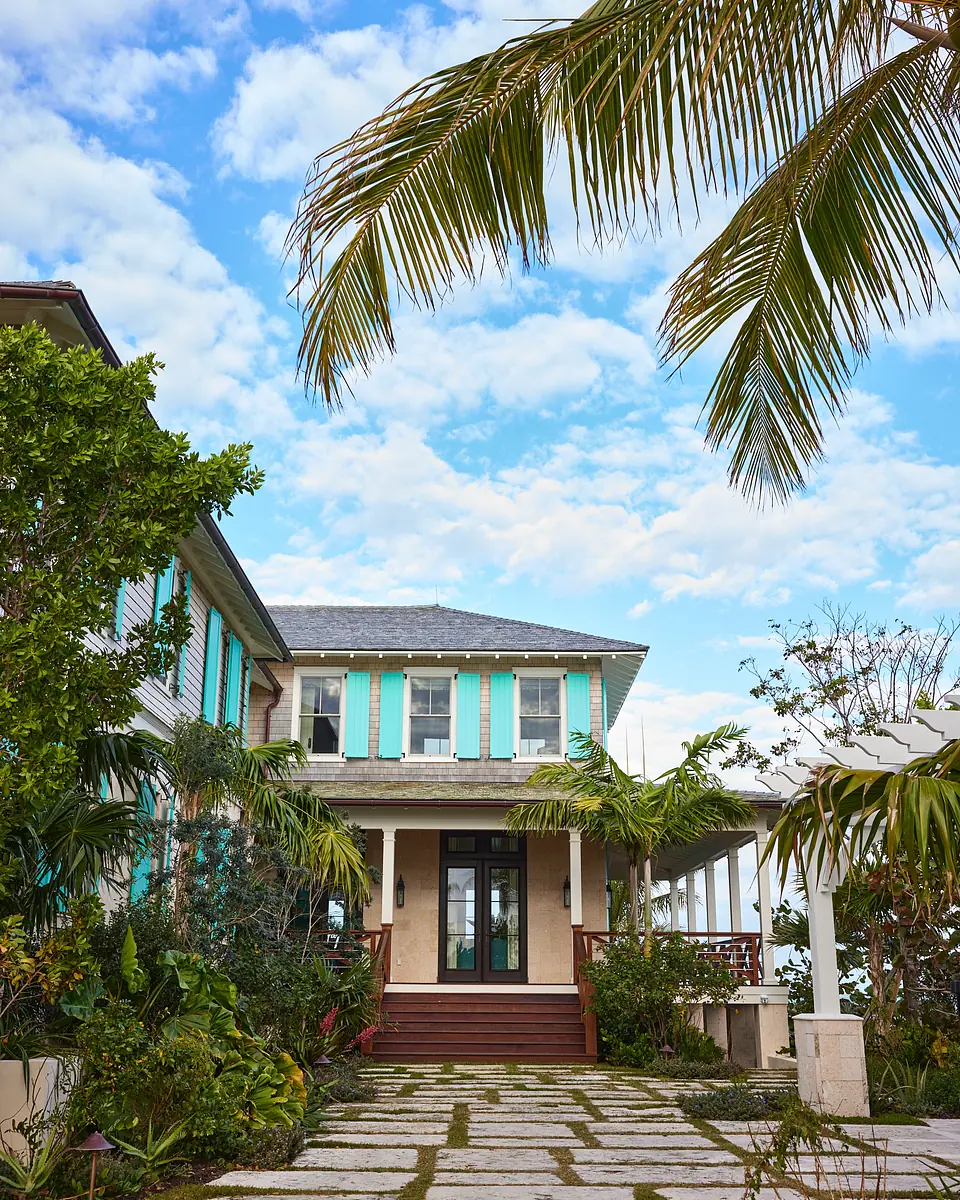 Exterior front of a house with turquoise shutters, porch, wooden stairway, and lush greenery.