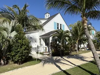 House exterior with white siding, blue shutters, palm trees, and a sandy path.