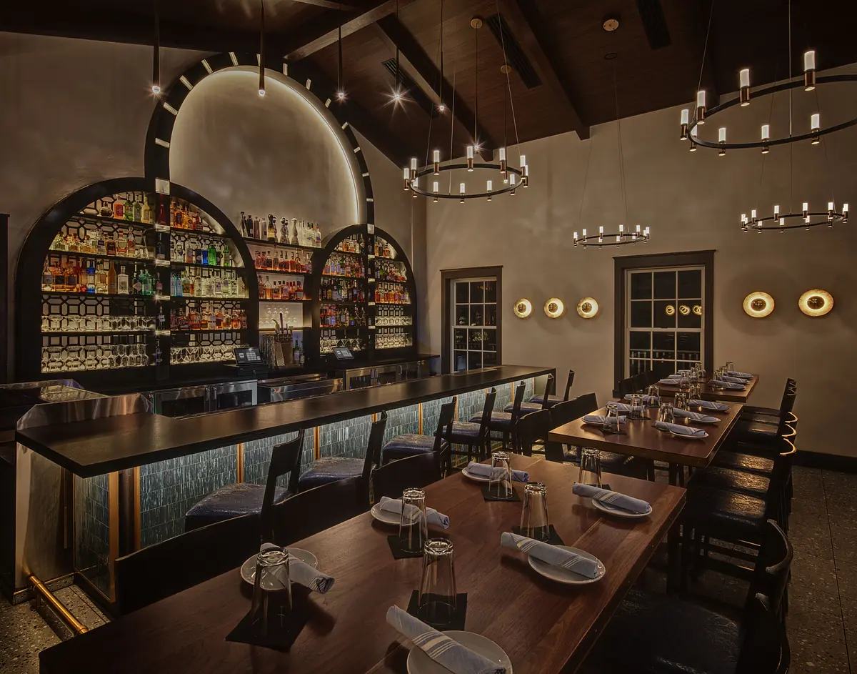 Dining room with long wooden table, black chairs, built-in bar, and circular chandeliers.